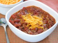 Homemade chili with beef and beans, garnished with shredded cheddar cheese