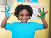 Smiling kid holding up his hands covered in paint