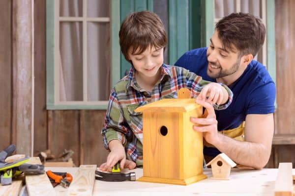 Man and son using woodworking tools to build a bird house