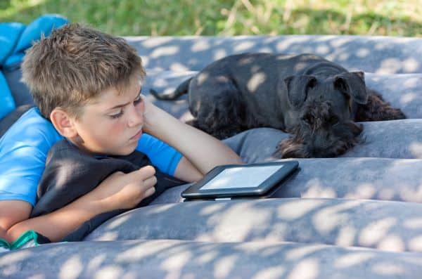 young boy reading an ebook outside with his dog