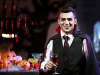 Young man dressed as vampire drinking cocktail at Halloween party