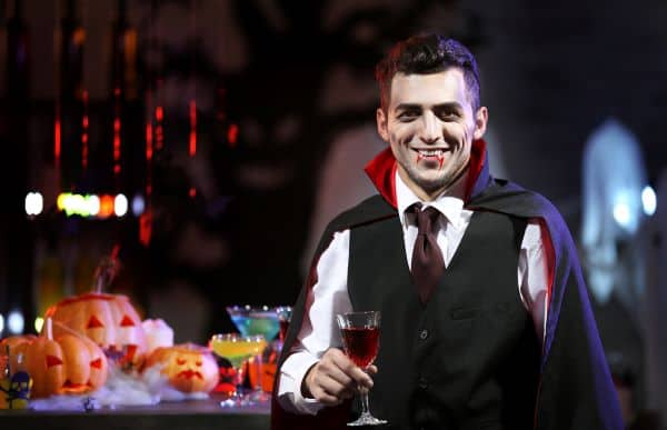 Young man dressed as vampire drinking cocktail at Halloween party