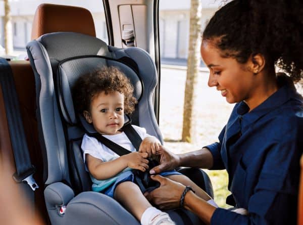 mom fastening child in car seat