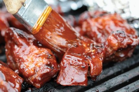 brushing barbecue sauce on grilled ribs