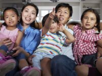 Asian Family Sitting On Sofa Watching TV Together