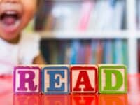 colorful block spell 'read' in front of happy child and bookcase