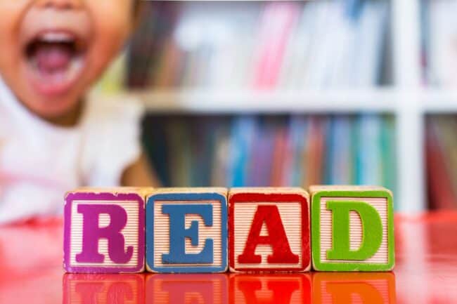 colorful block spell 'read' in front of happy child and bookcase